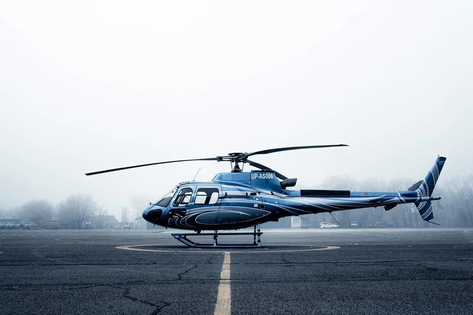 Side view of a dark blue Airbus AS350 helicopter parked on a foggy helipad